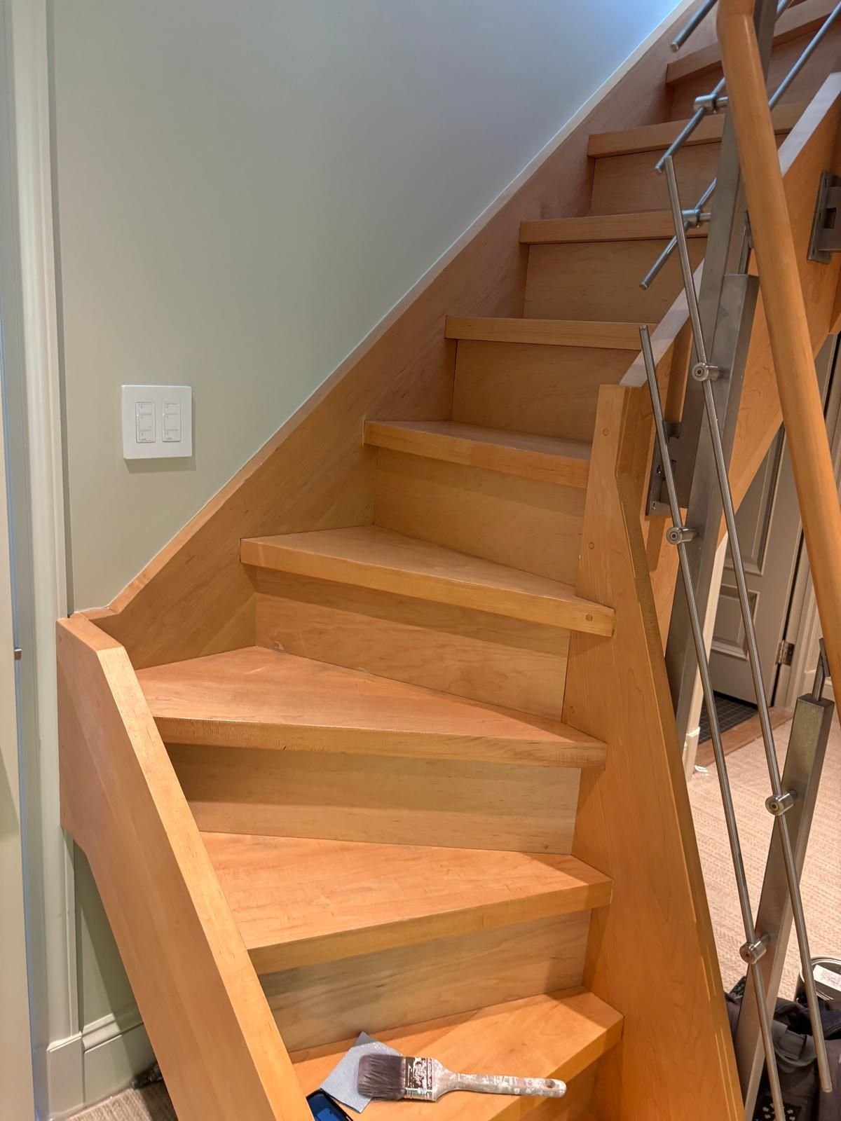 Cutting in fresh wall paint beside a wood staircase